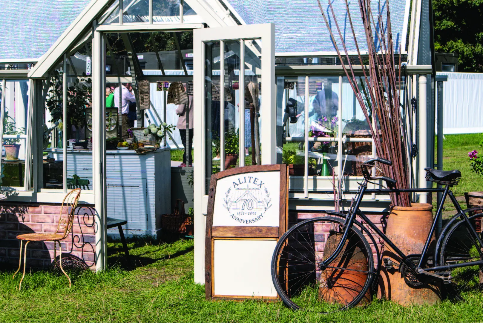 Alitex National Trust Mottisfont Greenhouse at Goodwood Revival, styled with an old vintage bike and car door at the front, with a large ceramic pot filled with sticks.